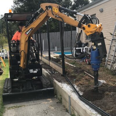 Digging postholes with Excavator above retaining wall.
